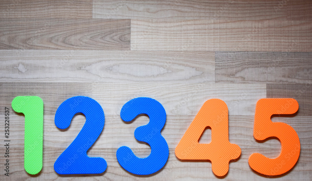Colorful numbers from one to five in row on light brown wooden texture laminate floor background indoors with copy space. Educational children toys for learning colors and numbers concept. Colorful numbers from one to five in row on light brown wooden texture laminate floor background indoors with copy space. Educational children toys for learning colors and numbers concept.
