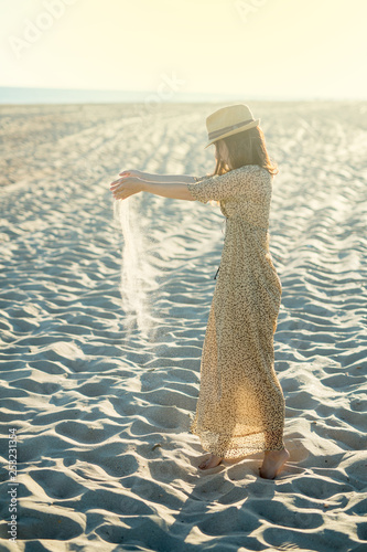 girl in a beautiful dress is pouring sand from her hands. Beautiful sunset on the beach. Concept - hipster.