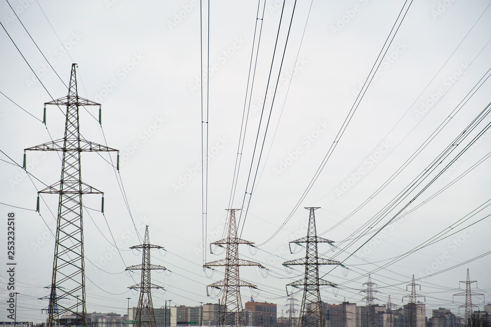 Power lines with many wires and metal supports on the open water against the sky. The concept of a modern city in the background and a lot of electrical wires in the foreground