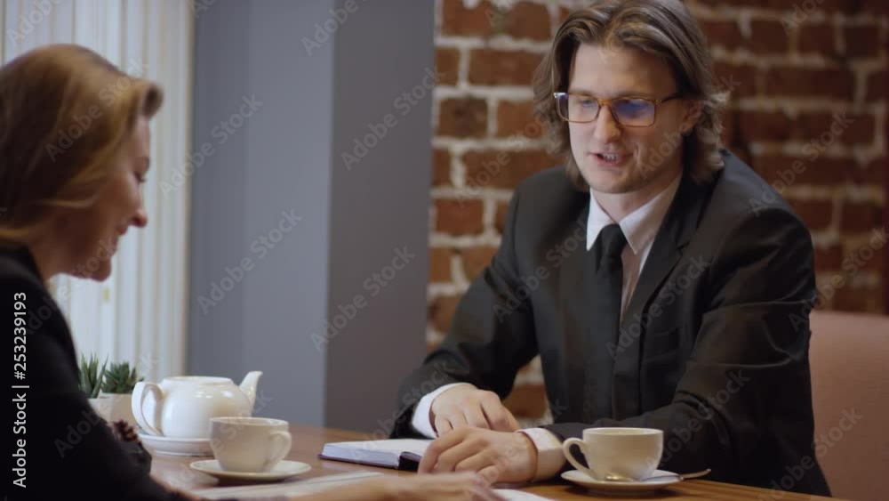 Two young people are working together and discussing projects in a cafe. The woman and the man in a restaurant or a coffee shop are drinking coffee. It is a business meeting. The man pays the bill. Two young people are working together and discussing projects in a cafe. The woman and the man in a restaurant or a coffee shop are drinking coffee. It is a business meeting. The man pays the bill.