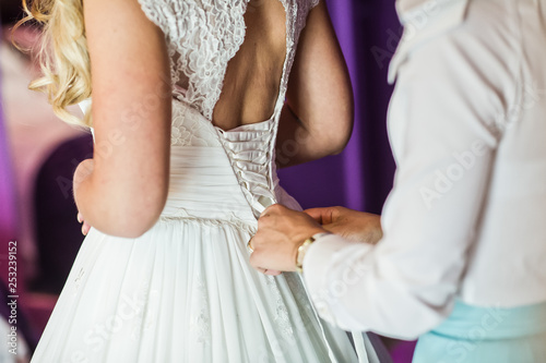 Bridesmaid helps to dress the bride wedding dress, hotel interior, purple background