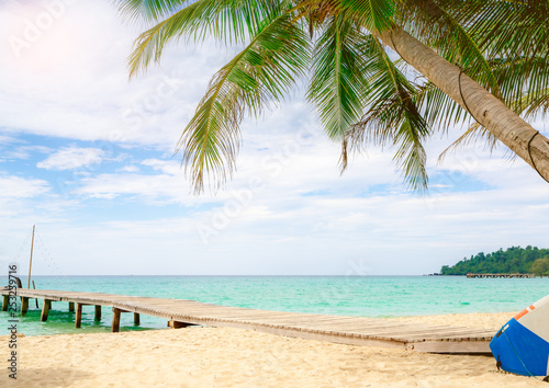 Beautiful view tropical paradise beach of resort. Coconut tree, wooden bridge, and kayak at resort on sunny day. Summer vacation concept. Summer vibes. Golden sand beach of resort with blue sky.