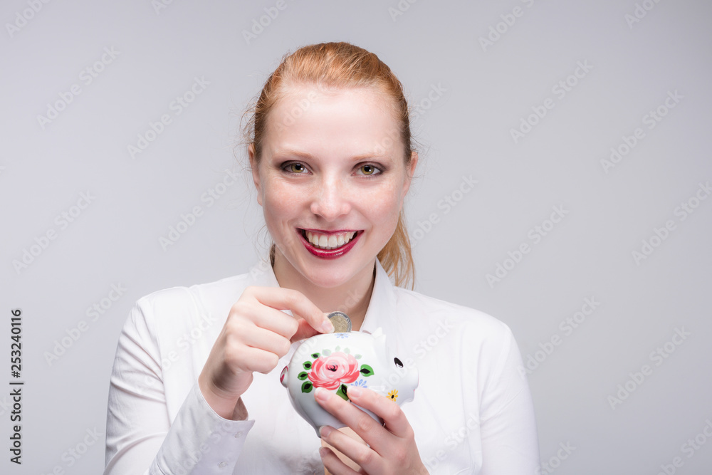 young red haired and happy woman puts a coin into her piggy bank young red haired and happy woman puts a coin into her piggy bank