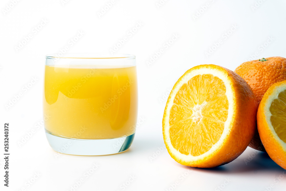 Orange juice in a clear glass cup with fresh oranges.