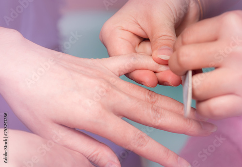 Woman receiving fingernail manicure service by professional  manicurist at nail salon. Beautician file nail manicure at nail and spa salon. Hand care and fingernail treatment at nail salon.
