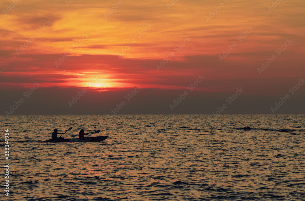 Silhouette of couples are kayaking in the sea at sunset. Kayak in the tropical sea at sunset. Romantic couple travel on summer vacation. Adventure activities of romantic couples.  Beautiful sunset sky