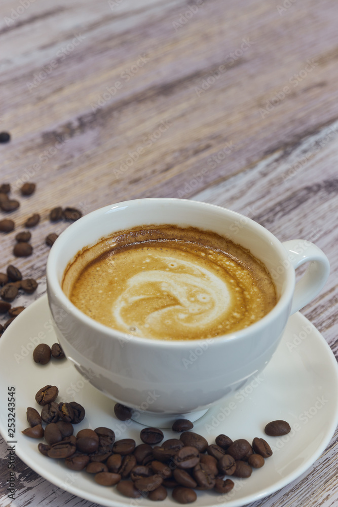 white cup with black coffee with milk. Handful of coffee beans on a wooden table. vertical view of drink with coffee. Copy space close up. white cup with black coffee with milk. Handful of coffee beans on a wooden table. vertical view of drink with coffee. Copy space close up.