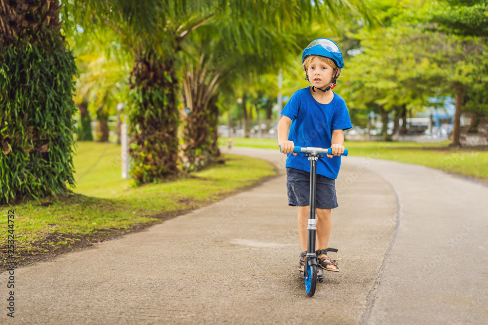 Fototapeta premium Boy riding scooters, outdoor in the park, summertime. Kids are happy playing outdoors