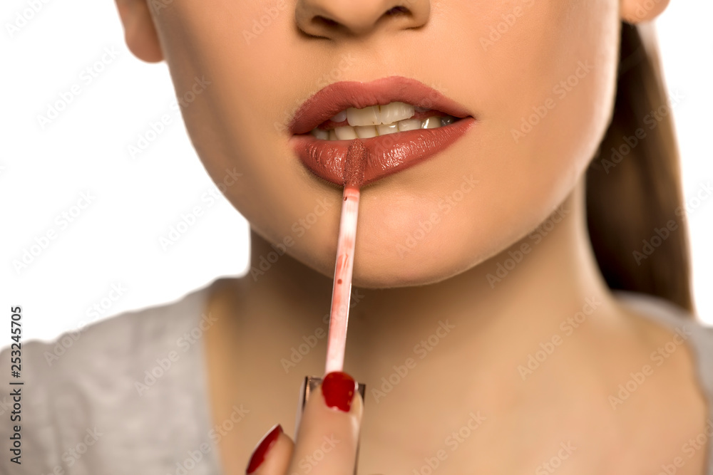 Young woman applying lip gloss on white background Young woman applying lip gloss on white background
