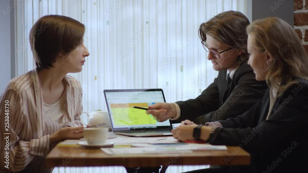 Three people are working together and discussing a contract in a cafe. The women and the man in a restaurant or a coffee shop are drinking coffee. It is a business meeting. They're working on business Three people are working together and discussing a contract in a cafe. The women and the man in a restaurant or a coffee shop are drinking coffee. It is a business meeting. They're working on business