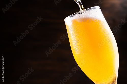 Cold beer is pouring into a glass forming foam.