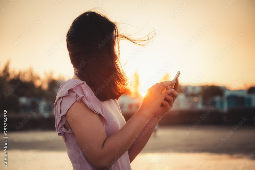 Portrait of Woman is Using Smartphone at The Beach Duration Summer Vacation, Asian Tourist is Relaxing With Her Cell Phone on The Beach in Holiday Time. Technology Communication Concept.