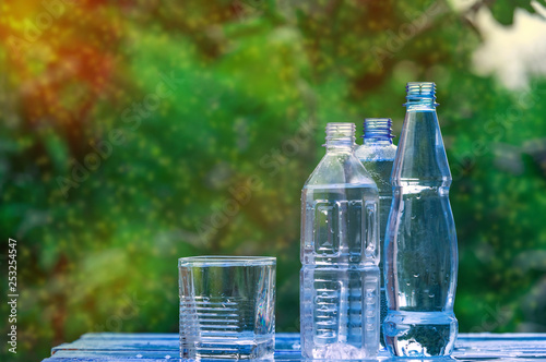 Bottle and glass of cool fresh water on nature background. Glass of water on table. Splash in glass. Healthy life concept. Pouring Water into a Glass