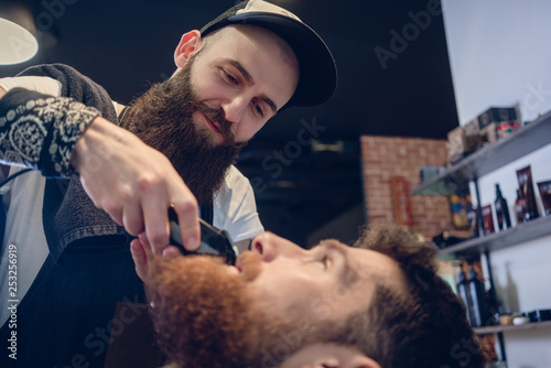 Head of a man and the hand of a barber trimming his beard