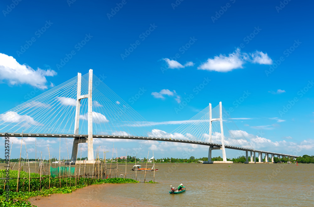 Fototapeta premium Dong Thap, Vietnam - January 17th, 2019: Fishermen are fishing in a small boat in the middle of the river, a cable-stayed bridge that represents the economic development in Dong Thap, Vietnam.