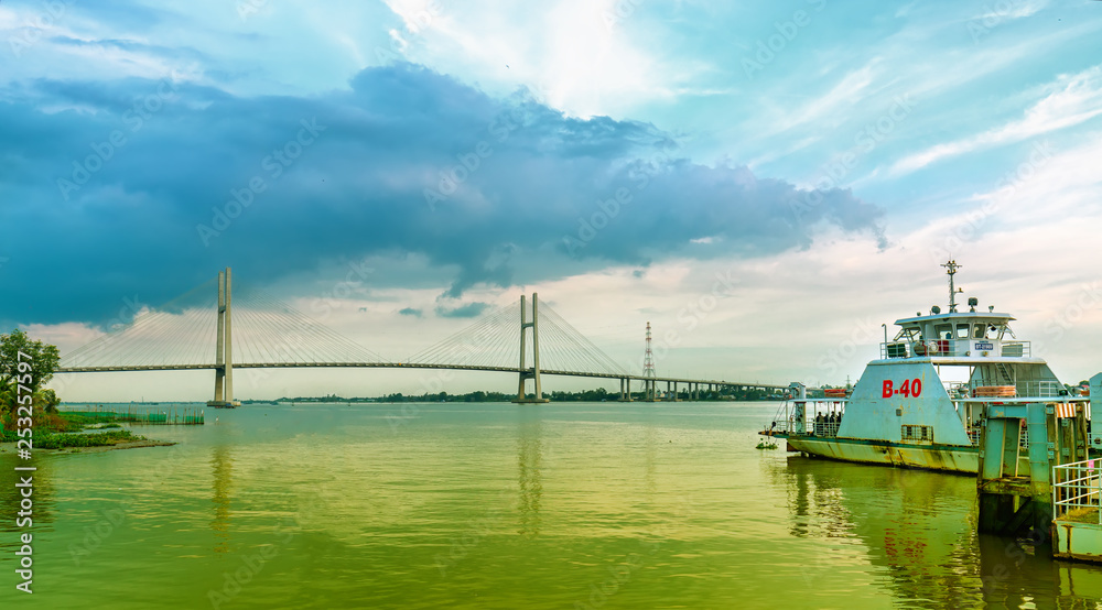 Fototapeta premium Dong Thap, Vietnam - January 16th, 2019: Landscape ferry about to leave port to transport passengers across Mekong river in spring, far away is Cao Lanh bridge just completed in Dong Thap, Vietnam.