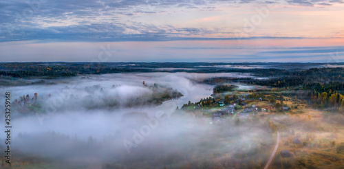 Foggy panorama of the village on the lake. Autumn dawn. Fog over the village, houses, village. On the shore of the lake in the fog.