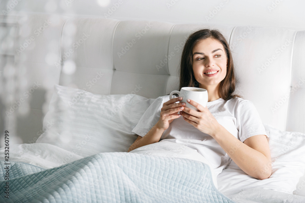 Brunette girl drinking coffee at the bed