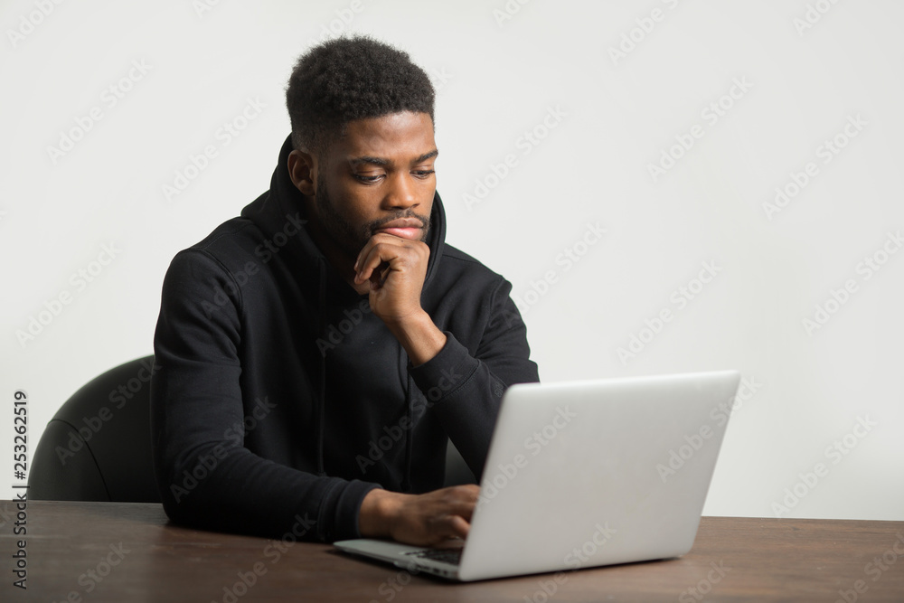 handsome african man in a tracksuit sits at a table with a laptop handsome african man in a tracksuit sits at a table with a laptop