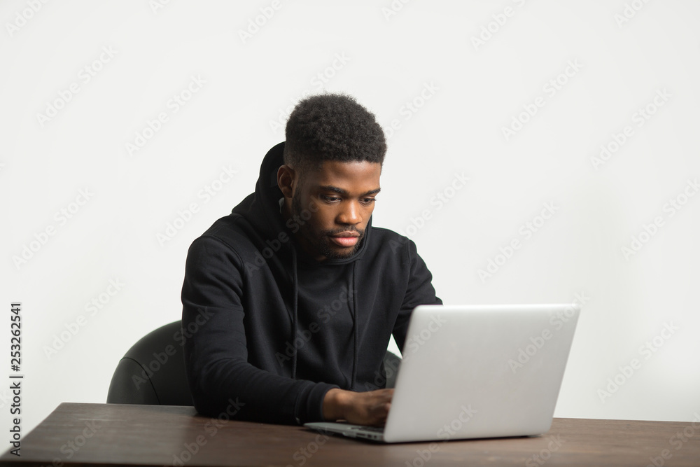 handsome african man in a tracksuit sits at a table with a laptop handsome african man in a tracksuit sits at a table with a laptop