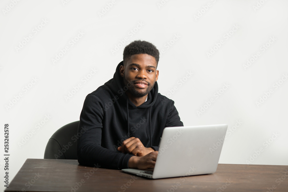 handsome african man in a tracksuit sits at a table with a laptop handsome african man in a tracksuit sits at a table with a laptop