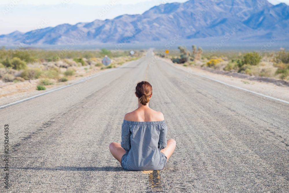 Young woman sitting on an endless straight empty road in the middle of nowhere on the Route 66 road. Backpackers, visionary, entrepreneur, adventure concepts.