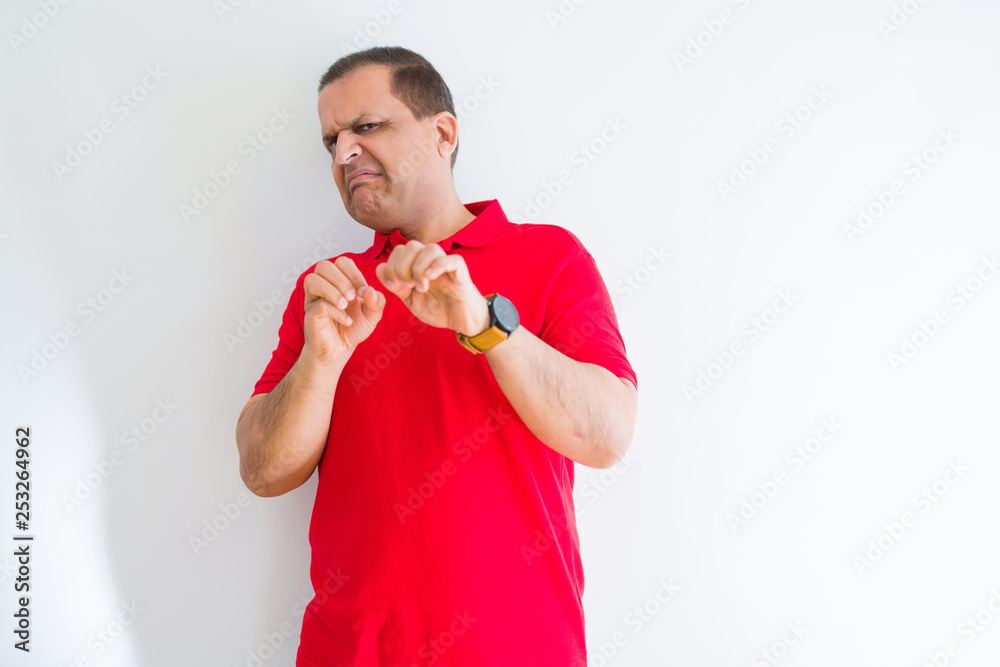 Middle age man wearing red t-shirt over white wall disgusted expression, displeased and fearful doing disgust face because aversion reaction. With hands raised. Annoying concept. Middle age man wearing red t-shirt over white wall disgusted expression, displeased and fearful doing disgust face because aversion reaction. With hands raised. Annoying concept.