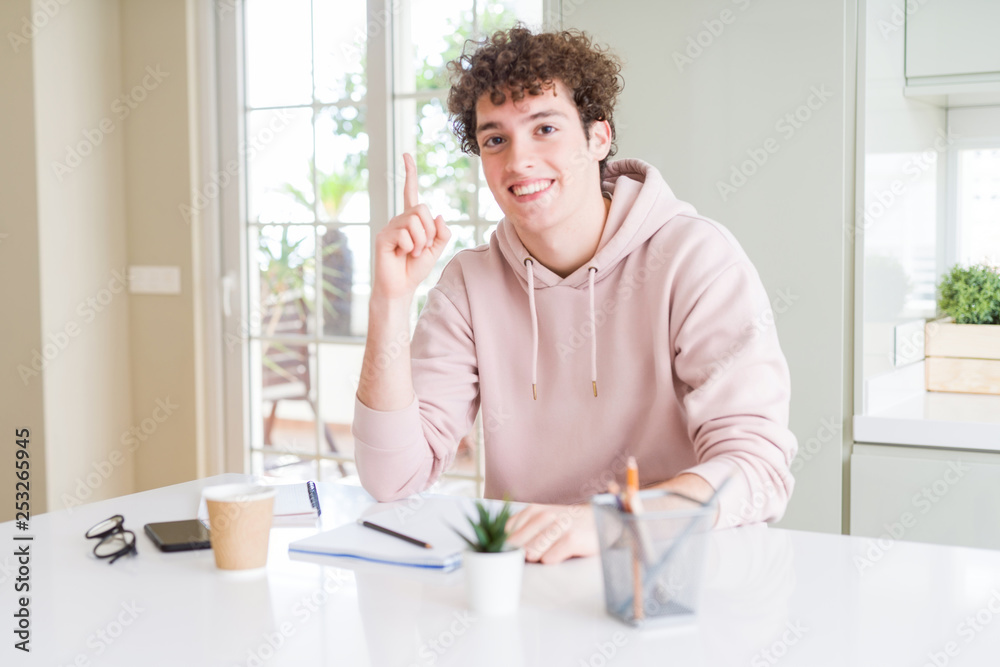 Young student man writing on notebook and studying pointing finger up with successful idea. Exited and happy. Number one. Young student man writing on notebook and studying pointing finger up with successful idea. Exited and happy. Number one.