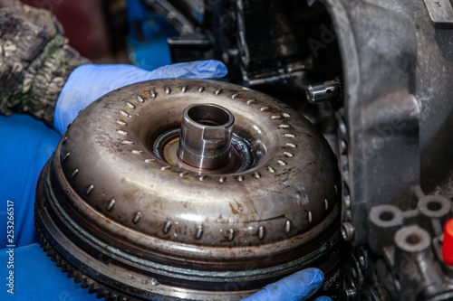 Canvas Print Close-up of a young male repairman in a working uniform repairing a torque converter and installing it in an automatic transmission of a supported car in an auto repair shop