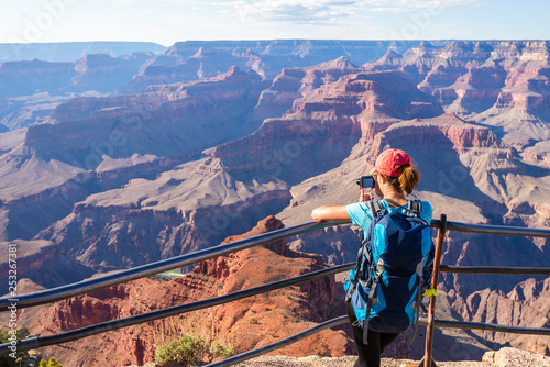 Young woman standing on the edge of Grand Canyon taking a photograph. Grand Canyon hiker woman resting. Hiking caucasian girl relaxing on  South rim of Grand Canyon, Arizona.