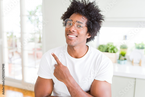 African American man wearing glasses cheerful with a smile of face pointing with hand and finger up to the side with happy and natural expression on face