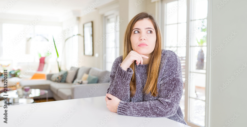 Beautiful young woman at home with hand on chin thinking about question, pensive expression. Smiling with thoughtful face. Doubt concept. Beautiful young woman at home with hand on chin thinking about question, pensive expression. Smiling with thoughtful face. Doubt concept.