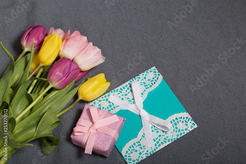 Bouquet of tulips of different colors on a gray background. Next greeting card and gift wrapped.
