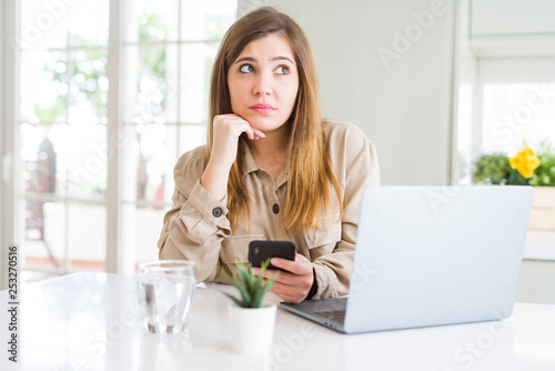 Beautiful young woman using smartphone and computer serious face thinking about question  very confused idea