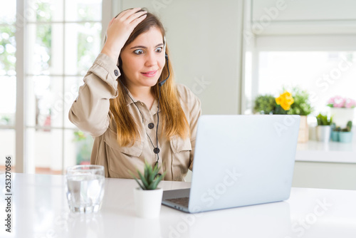 Beautiful young operator woman working with laptop and wearing headseat stressed with hand on head, shocked with shame and surprise face, angry and frustrated. Fear and upset for mistake.