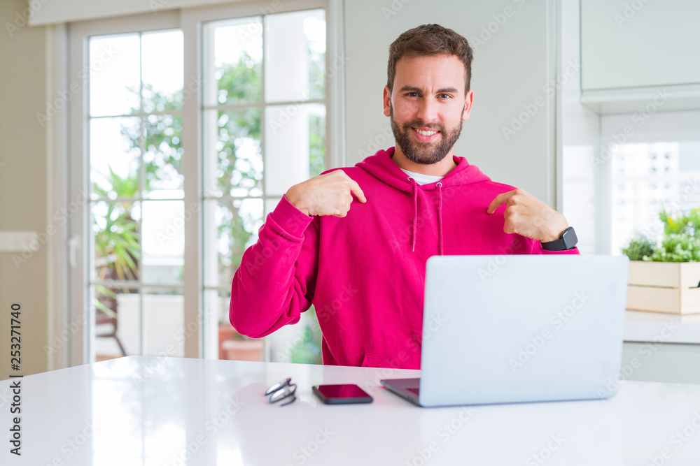 Handsome man working using computer laptop looking confident with smile on face, pointing oneself with fingers proud and happy.