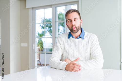 Handsome man wearing casual sweater making fish face with lips, crazy and comical gesture. Funny expression.