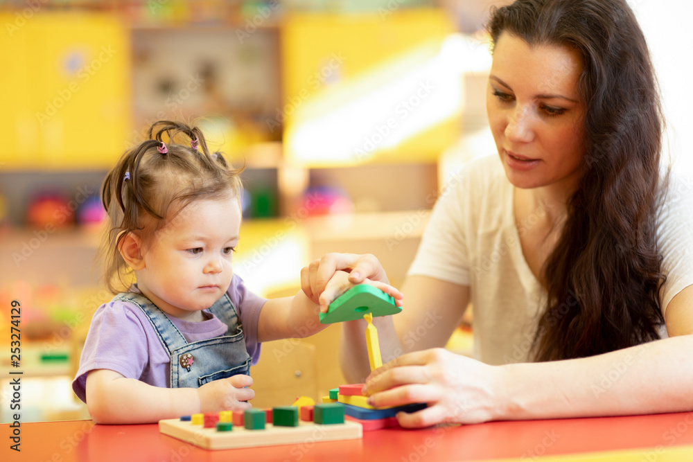 Teacher and baby one year ago playing logical toys in nursery Teacher and baby one year ago playing logical toys in nursery