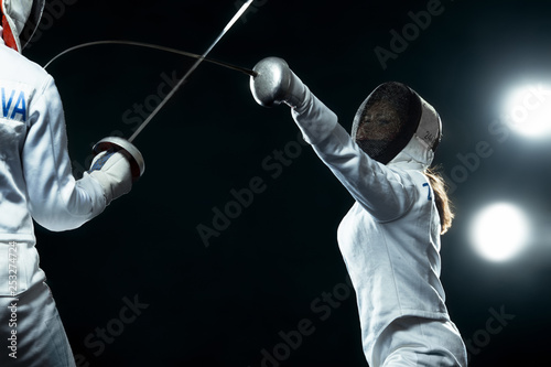 Young fencer athlete wearing mask and white fencing costume. holding the sword on black background with lights. photo