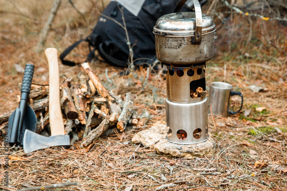 camping woodstove and utensils, axe and sapper shovel near a firewoods, backpack on the background camping woodstove and utensils, axe and sapper shovel near a firewoods, backpack on the background