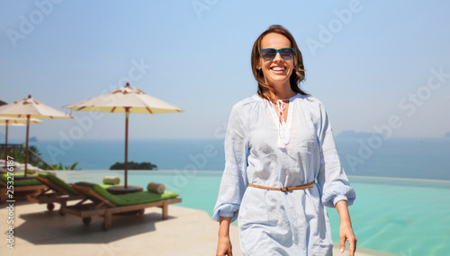 people and leisure concept - happy smiling woman walking over infinity edge pool of touristic resort background