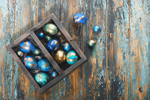 Painted colored Easter eggs in dark wooden box on dark wooden background. Boho stile.