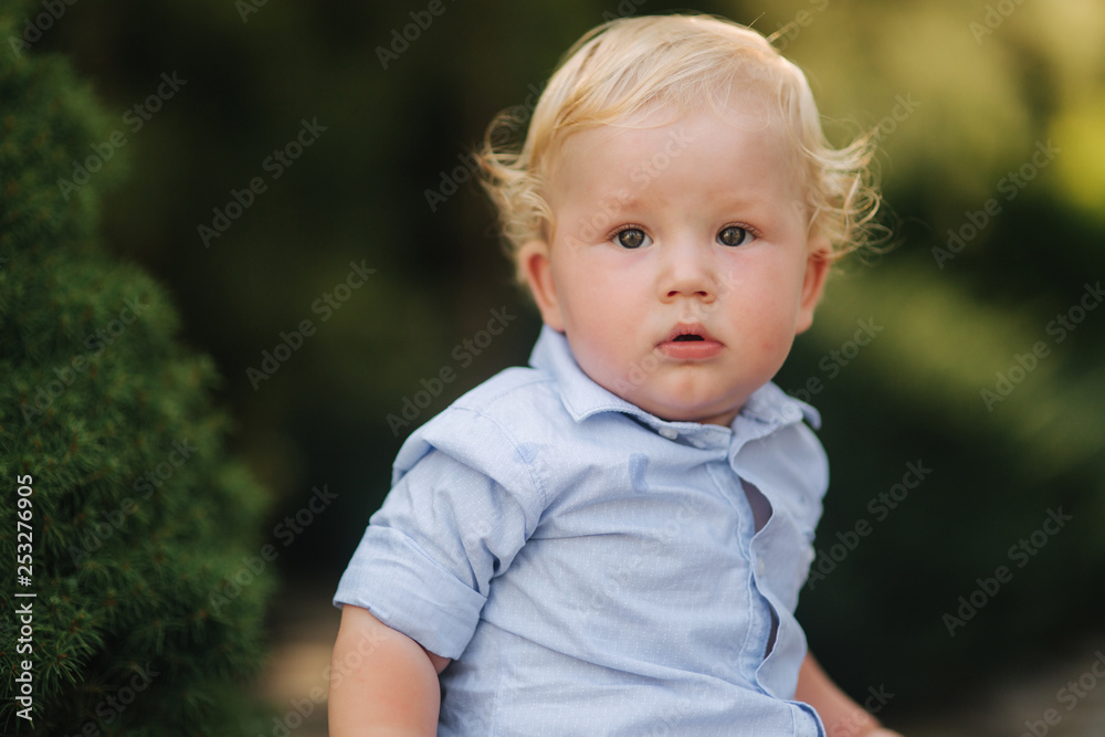 Happy little boy sit outside in summer time. Boy with curly blond hair Happy little boy sit outside in summer time. Boy with curly blond hair