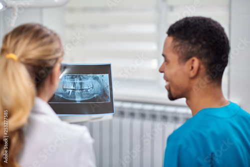 Caucasian female dentist explaining to african male rookie x-ray
