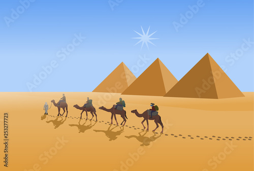 Four camel riders are hiking in the hot sun in the desert with pyramid and blue sky background.