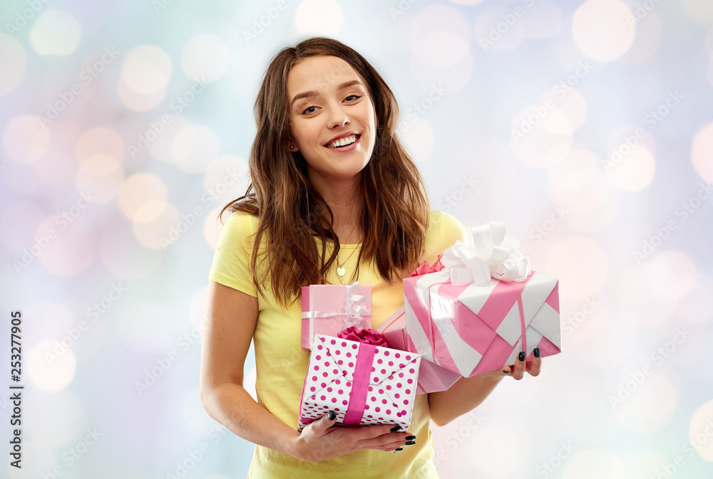 birthday and people concept - smiling young woman or teenage girl in yellow t-shirt with gift boxes over festive lights background birthday and people concept - smiling young woman or teenage girl in yellow t-shirt with gift boxes over festive lights background