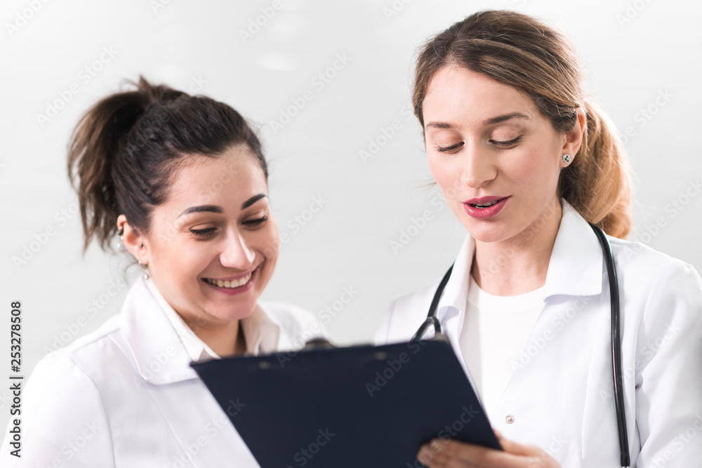 Two female assistants dressed in white coats talking to each other in the dentistry center Two female assistants dressed in white coats talking to each other in the dentistry center