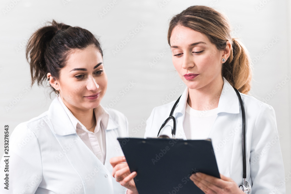 Two female assistants dressed in white coats talking to each other in the dentistry center Two female assistants dressed in white coats talking to each other in the dentistry center
