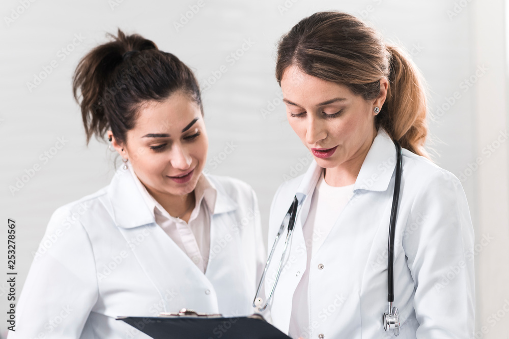 Two female assistants dressed in white coats talking to each other in the dentistry center Two female assistants dressed in white coats talking to each other in the dentistry center
