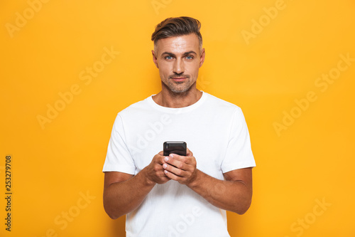 Handsome man posing isolated over yellow wall background using mobile phone.